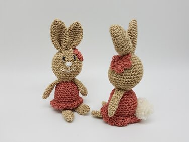 Zwei Ansichten eines gehäkelten Amigurumi-Hasen in Beige mit dunkelrosafarbenem Kleid, Häkelblume am Ohr und weißem Puschelschwanz