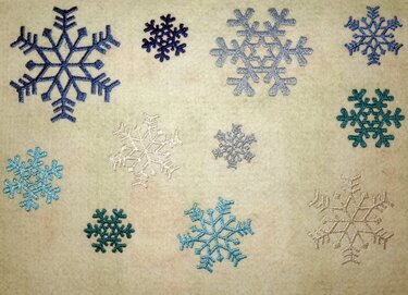 Verschiedene bestickte Schneeflocken in Blau, Türkis, Hellgrau und Weiß auf hellem Stoff