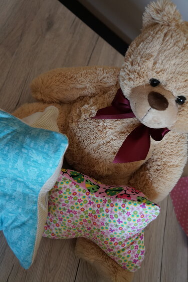 Geblümtes Leseknochenkissen und hellblaues Zierkissen neben einem Plüschteddy