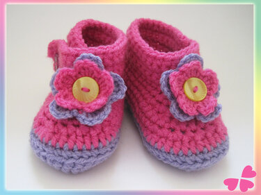 Nahaufnahme zweifarbiger gehäkelter Babyschuhe mit Blütenapplikation und Knopf
