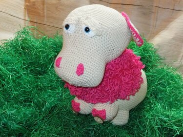 Gehäkeltes Amigurumi-Schaf in Creme mit pinker lockiger Wolle, sitzend auf grünem Dekogras