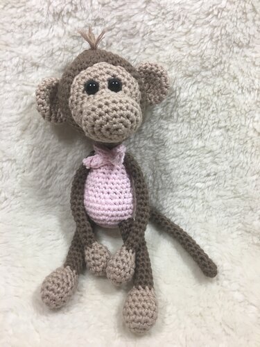 Handgehäkelter brauner Amigurumi-Affe mit rosafarbenem Bauch und Halstuch auf hellem Plüsch