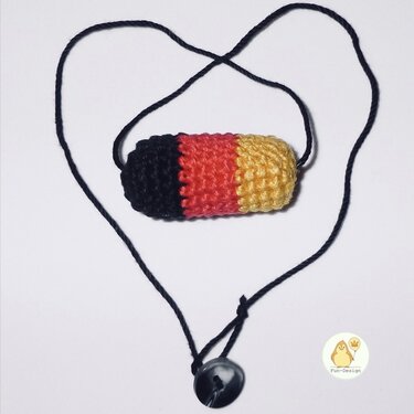 Gehäkelter zylindrischer Anhänger in Schwarz, Rot und Gold an schwarzer Kordel in Herzform mit Knopf.