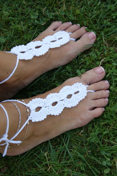 Weiße gehäkelte Barfußsandalen an Füßen auf grünem Gras
