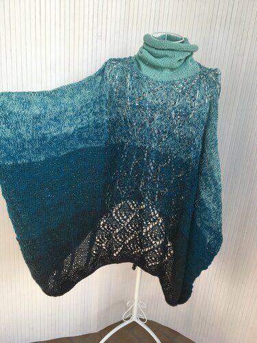 Gestrickter Poncho in Türkis-Petrol Ombre mit Rollkragen und Lochmuster auf einer weißen Schneiderpuppe.