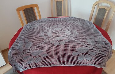 Quadratisches Filetdeckchen mit wiederkehrenden Blütenmustern auf rundem Tisch mit rotem Tischtuch