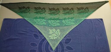 Dreieckiges Filet-Häkeltuch mit Blattmotiven und grün-schwarzem Farbverlauf, auf blauem Tuch ausgebreitet