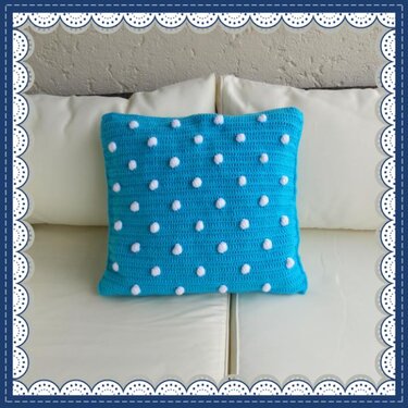 Türkises gehäkeltes Kissen mit weißen Noppen auf hellem Sofa