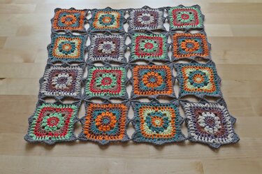 Handgehäkelte Decke aus bunten Granny Squares mit floralen Mustern auf hellem Holzboden