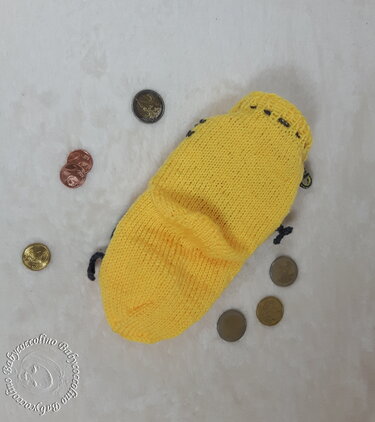 Gelbes gestricktes Münzetui mit Kordel auf hellem Untergrund und verstreuten Münzen