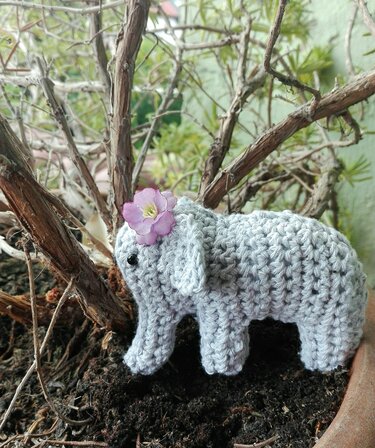 Kleines graues Amigurumi‑Elefant mit Stoffblume auf Erde im Topf