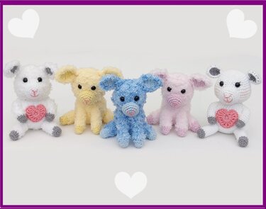 Fünf gehäkelte Amigurumi-Lämmer in Weiß, Gelb, Blau und Rosa, sitzend; zwei mit rosa Herz-Applikationen auf der Brust.