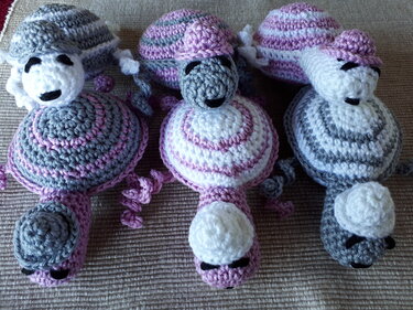 Drei gehäkelte Babyspielzeug-Figuren in Rosa, Grau und Weiß mit Spiralmuster