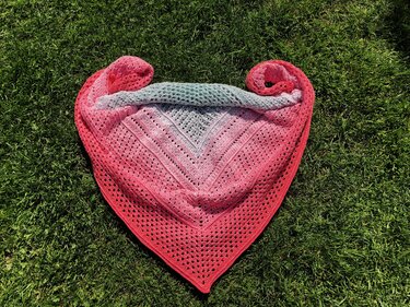 Gehäkeltes Dreieckstuch mit Farbverlauf von Grau zu Rosa und Koralle auf Gras