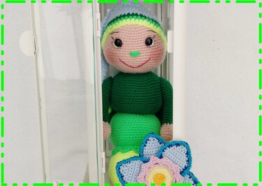 Gehäkelte Amigurumi-Puppe mit grünem Körper, blauer Zipfelmütze und gehäkelter Blume