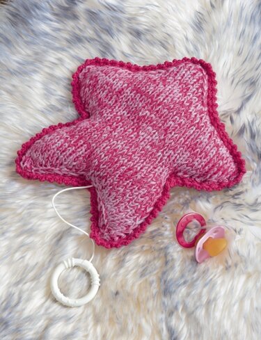 Kuscheliges rosa-weißes Sternkissen mit pinker Kante, Zugschnur und Schnuller auf hellem Felluntergrund