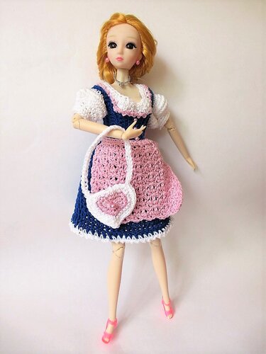 Modepuppe trägt gehäkeltes dunkelblaues Kleid mit rosa Schürze und herzförmiger Tasche