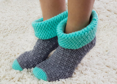 Pair of gray and aqua crochet ankle socks with folded aqua cuffs and contrast aqua toes on a cream rug