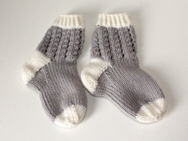 Paar gestrickter Babysocken grau-weiß mit Lochmuster am Schaft