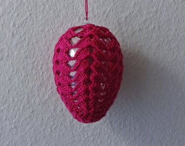 Nahaufnahme: pinke Häkelhülle mit Aufhänger um Osterei