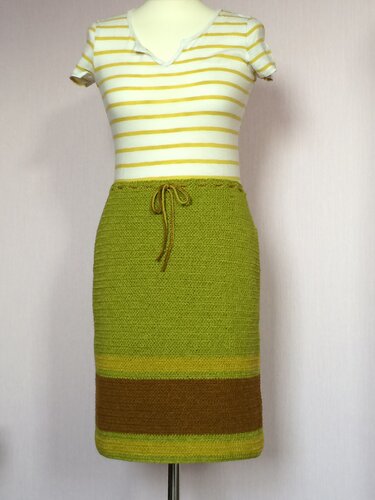 Knielanger gehäkelter Rock in Grün mit braunem und gelbgrünem Saumstreifen und Kordelzug, auf einer Schaufensterpuppe.