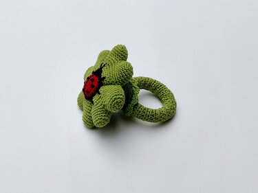 Gehäkelter grüner Blumen-Greifring mit rotem Marienkäfer in der Mitte, ideal für Babys