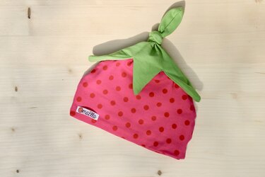 Pink gepunktete Babymütze mit grünem Blattabschluss auf hellem Holz