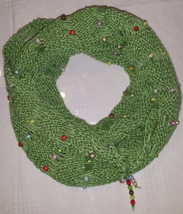 Grüner gestrickter Loop-Schal mit bunten Perlen auf hellem Untergrund