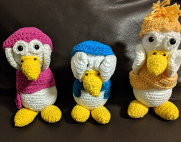 Drei gehäkelte weiße Enten mit gelben Schnäbeln und farbigen Mützen (pink, blau, orange)