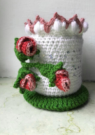 Weißer gehäkelter zylindrischer Behälter mit grüner Basis, dekoriert mit roten Rosen, grünen Blättern und dezenten Glitzerakzenten