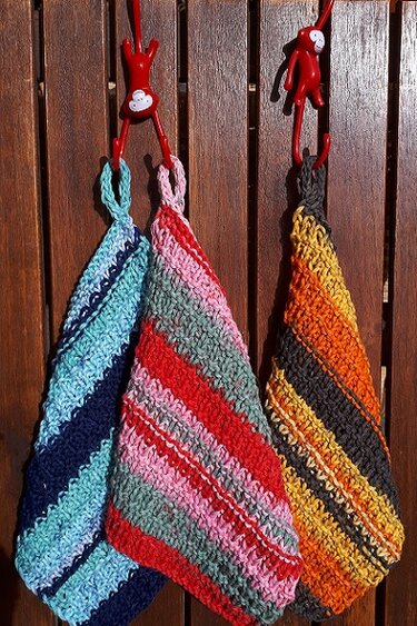 Drei gestrickte Tücher mit Streifenmustern an roten Haken vor einer Holzwand