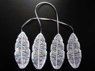 Vier bestickte Blattformen mit weißer Spitze und mintfarbenen Akzenten, verbunden durch ein schmales Band