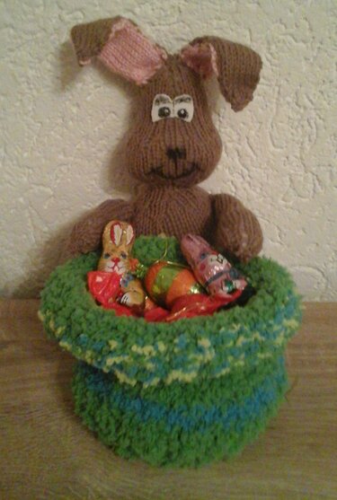 Gestrickter brauner Hase mit Schlappohren und grünem Körbchen voller Osterfiguren