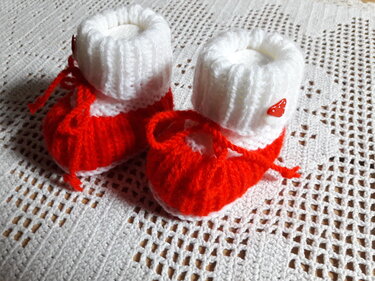 Rot-weiße gestrickte Babyschuhe mit Pilz-Knopf auf weißer Häkeldecke