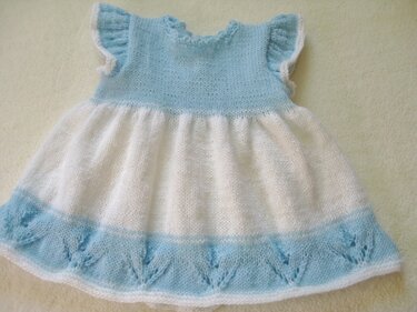 Hellblau-weißes gestricktes Babykleid mit Rüschenärmeln und Lochmuster am Saum