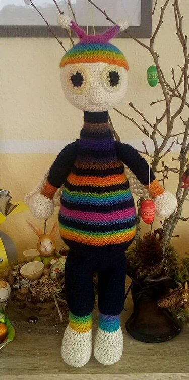 Gehäkelte Amigurumi-Figur mit Regenbogenstreifen, Antennen und großen Augen, stehend