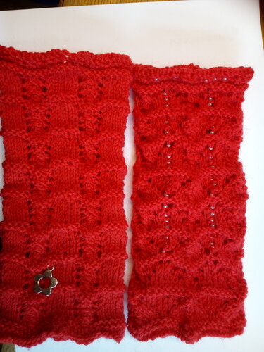 Zwei rote gestrickte Armstulpen mit Lochmuster, Perlenreihe und gezacktem Rand auf weißem Hintergrund