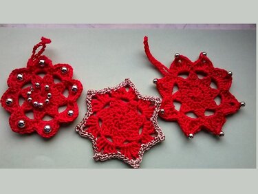 Drei rote gehäkelte Weihnachtsanhänger in Stern- und Blumenform mit silberfarbenen Perlen und Schlaufen