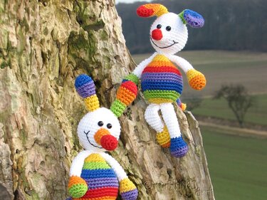 Zwei Amigurumi-Hasen in Regenbogenfarben auf einem Baumstamm.