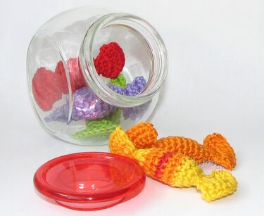 Gehäkelte Bonbons in einem Glas mit rotem Deckel daneben.