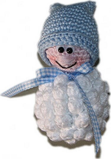 Gehäkelte Amigurumi-Figur in Weiß und Hellblau mit Mütze und kariertem Halstuch auf weißem Hintergrund.