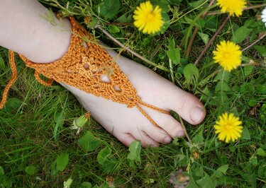 Fuß mit gehäkelter Barfußsandale in Terrakotta auf grüner Wiese mit gelben Blumen