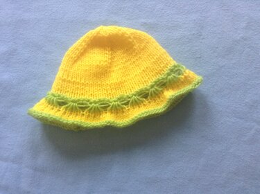 Gestrickter gelber Kinderhut mit grünem Muschelmuster am Rand auf blauem Stoff.
