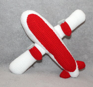 Zweifarbiges gehäkeltes Amigurumi-Flugzeug in Rot und Weiß auf grauem Hintergrund