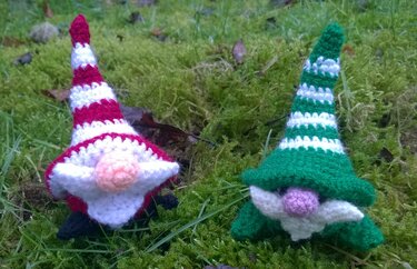 Zwei gehäkelte Amigurumi-Wichtel mit gestreiften Mützen auf Moos