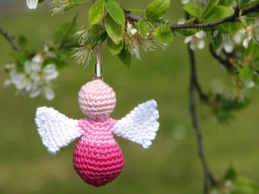 Gehäkelter Engel in Pink mit weißen Flügeln an blühendem Zweig hängend.