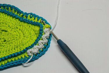 Nahaufnahme eines Häkelrands in Neongrün und Türkis mit weißem Zierstich und einem Häkelhaken.
