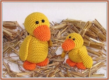 Gehäkelte gelbe Ente und kleines Küken nebeneinander auf Stroh