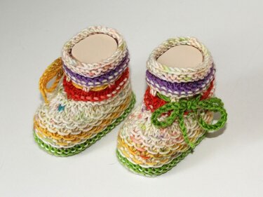Zwei handgestrickte Babyschuhe mit bunten Streifen, links mit gelber, rechts mit grüner Schleife.