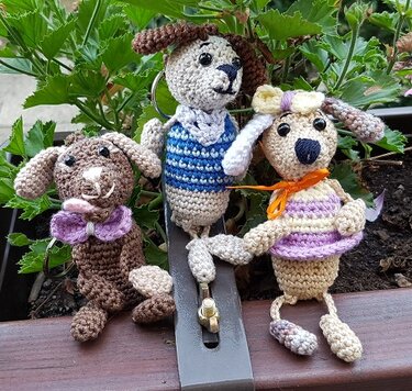 Drei gehäkelte Hunde-Amigurumis, einer mit Schlüsselring, ausgestattet mit kleinen Accessoires wie Fliege und Halstuch